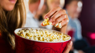 Kvinna äter popcorn ur stor bägare.