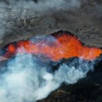 Vulkankrater med röd lava och vit rök som strömmar ut.