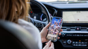 Bilförare håller i sin mobiltelefon.