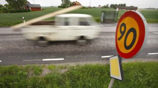 90-skylt bredvid väg där mindre lastbil susar förbi.