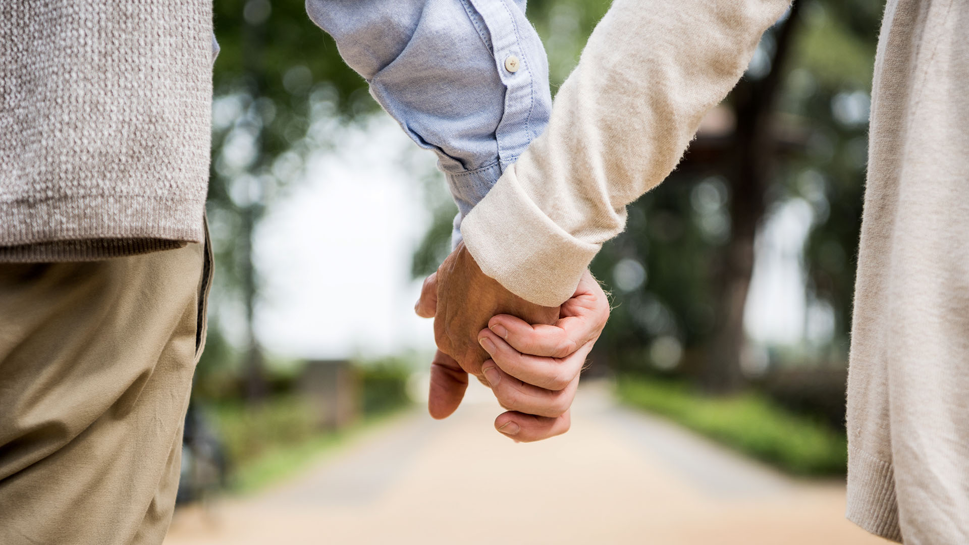 Äldre par promenerar utomhus hand i hand.