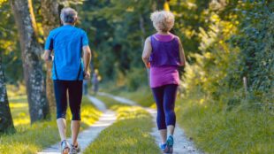Två seniorer joggar i en skog