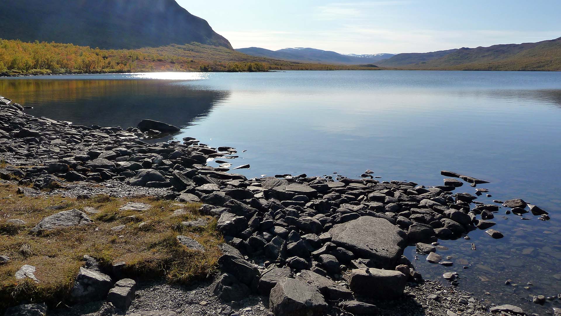 Fjällsjö med spegelblankt vatten och berg i bakgrunden.