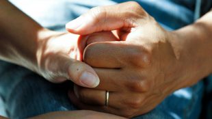 Två personer håller varandras hand, händer i närbild.