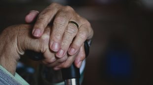 Händer på en gammal person. Händerna vilar över skaftet på en käpp.