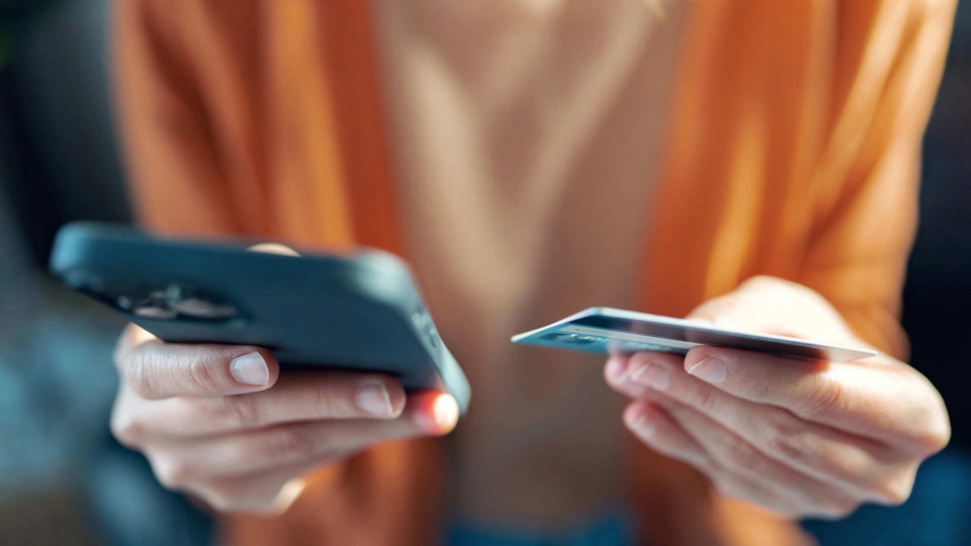 Kvinna i orange tröja betalar med kort i mobilen.