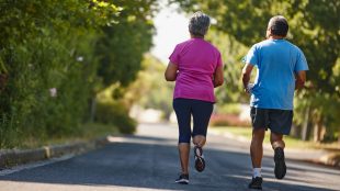 Två äldre personer joggar i lummig omgivning.